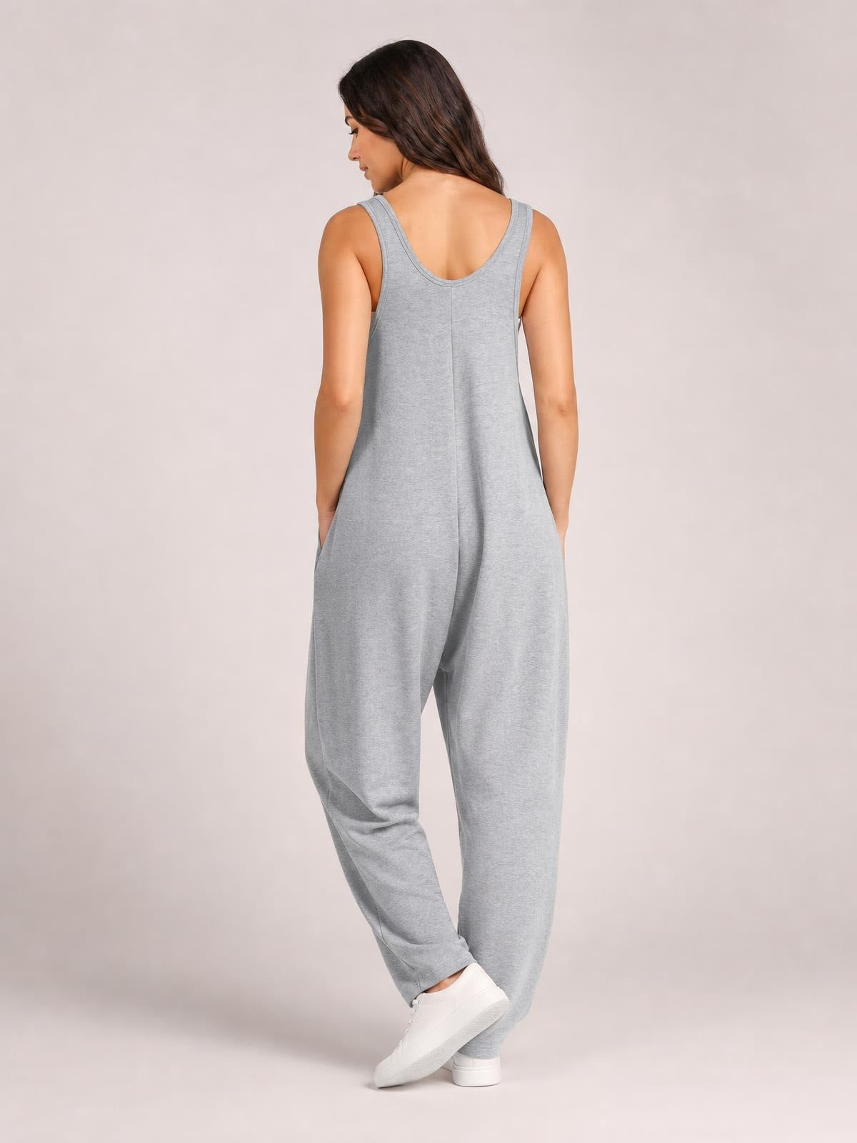 Model poses from the back in light gray V-neck wide strap overalls with side pockets, a relaxed loose silhouette, and tapered legs.