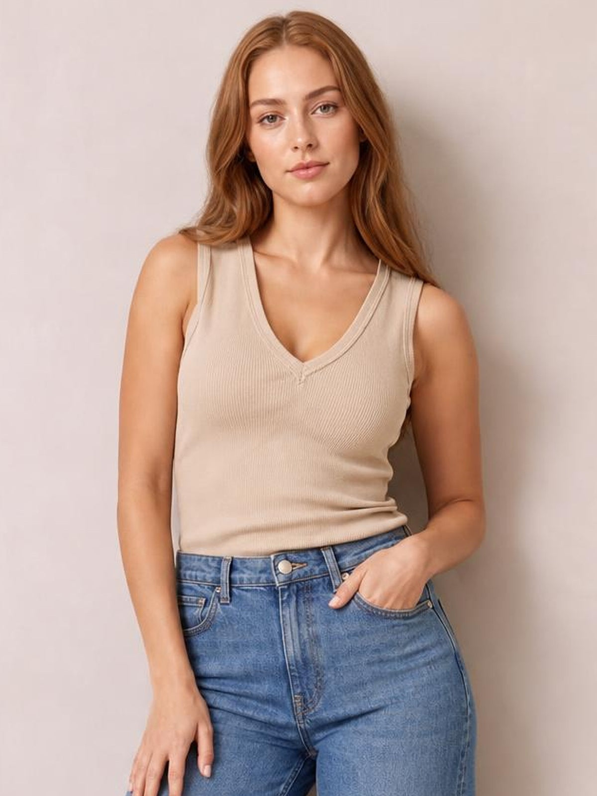 Model wearing a beige ribbed V-neck wide strap tank with a fitted silhouette, subtle stretch, and clean neckline binding, posing with one hand in her jeans pocket.