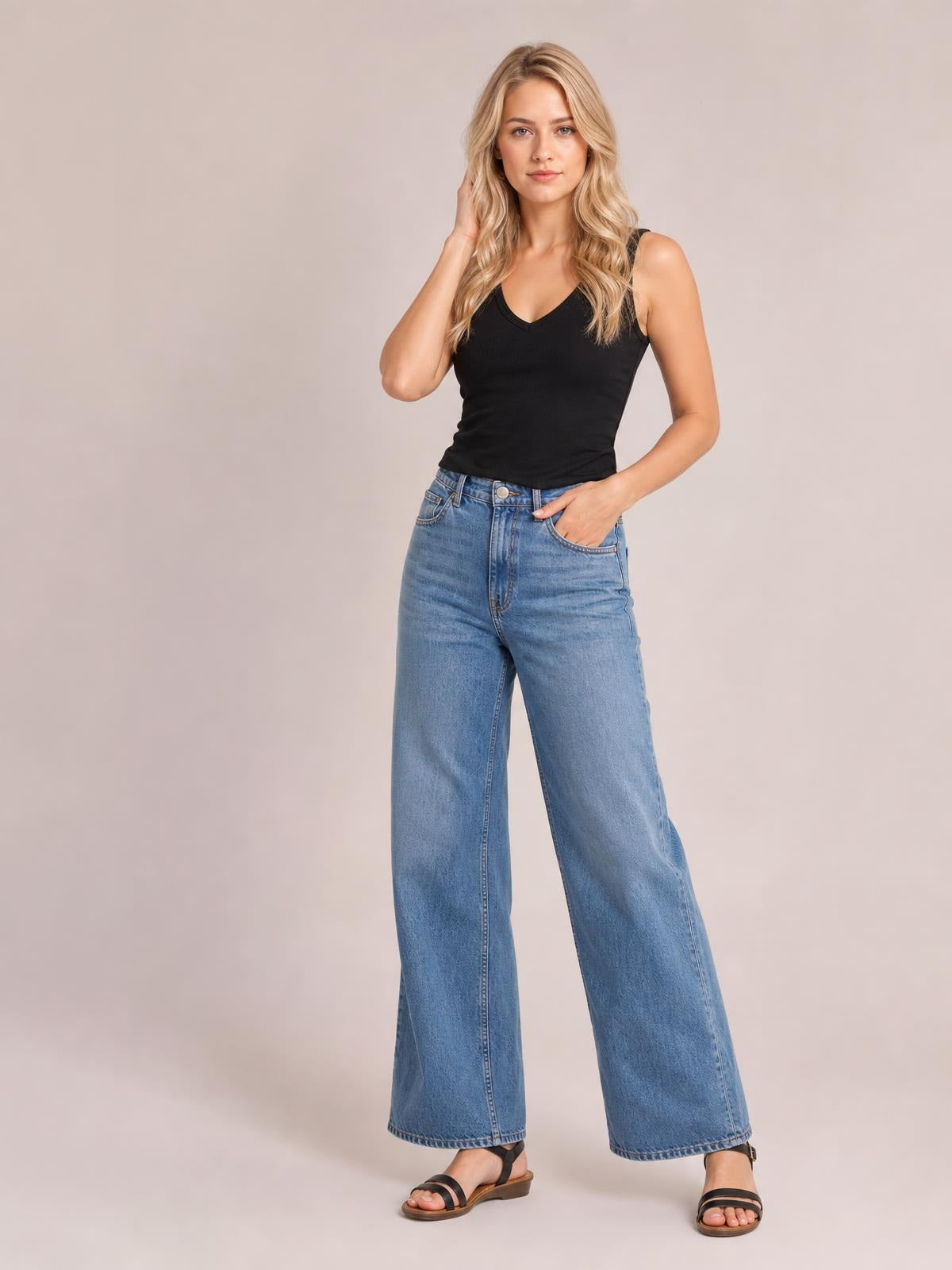 Model poses in a black V-neck wide strap tank with a fitted silhouette and subtle stretch, paired with light-wash wide-leg jeans.