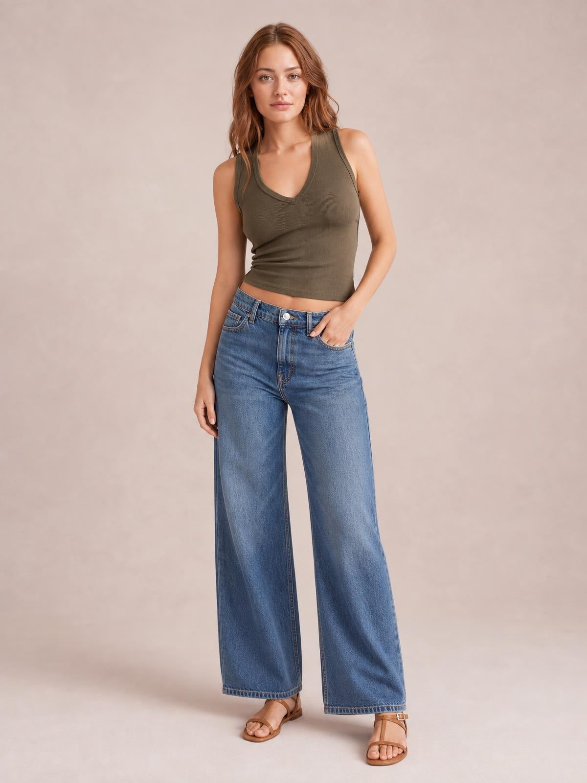 A model stands with one hand in her jeans pocket wearing an olive V-neck wide strap tank with a fitted, ribbed silhouette and double-stitched neckline.