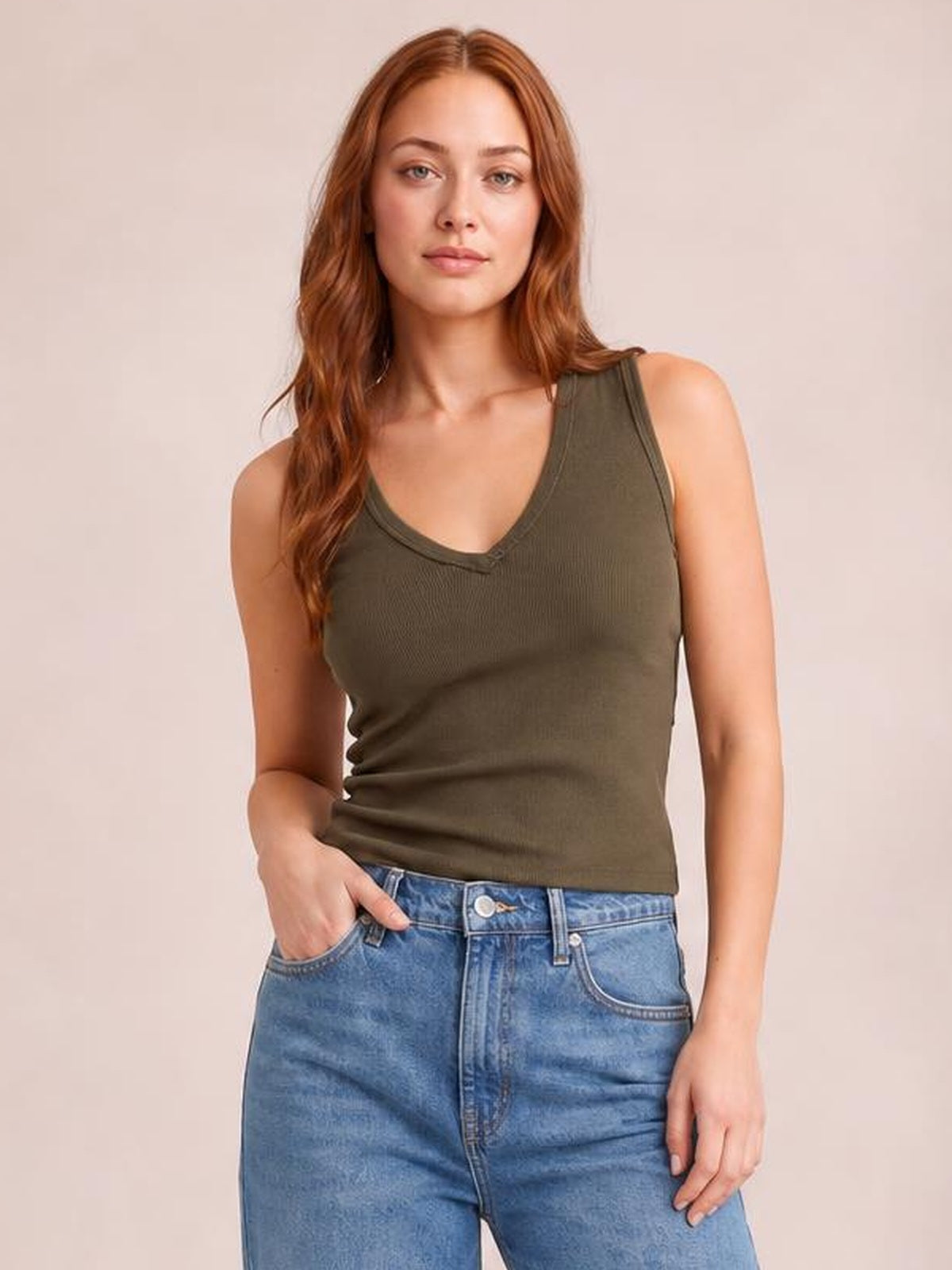 Model wearing an olive green V-neck wide strap tank with a fitted, slightly stretchy silhouette and neat neckline trim, paired with blue jeans.