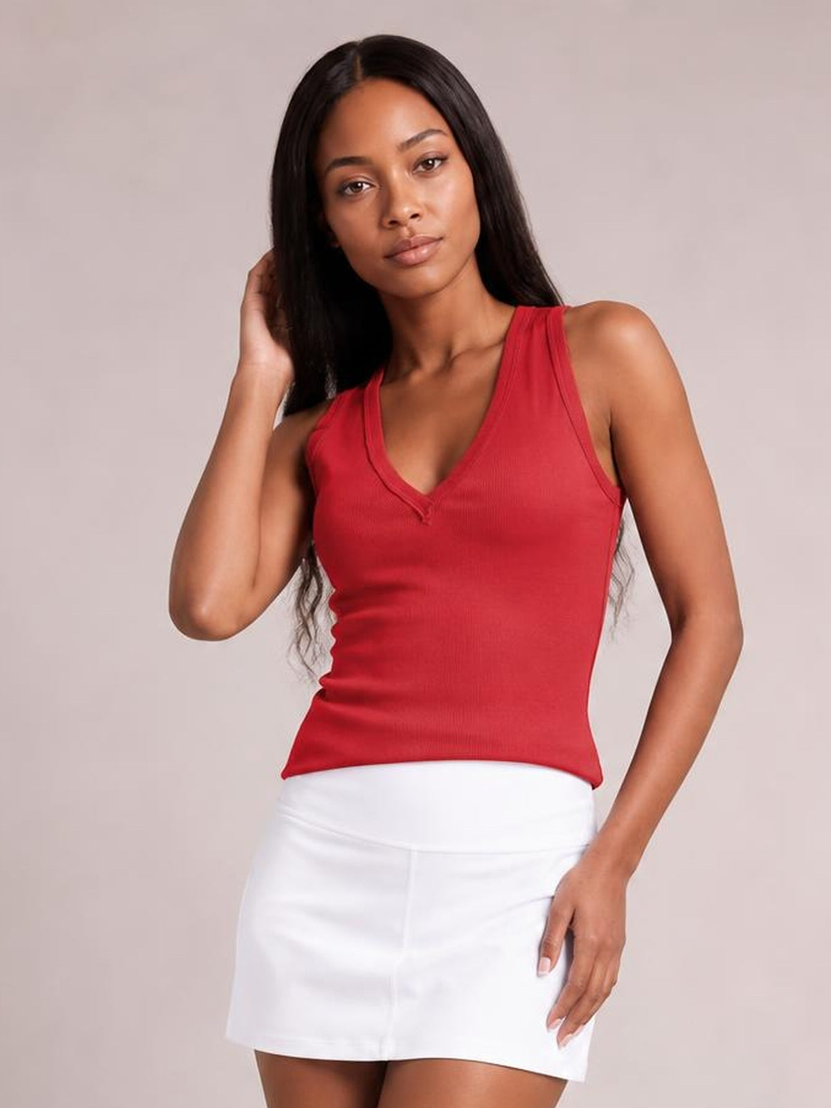 Model poses in a red V-neck wide strap tank with a fitted silhouette and subtle stretch, paired with a white skirt.