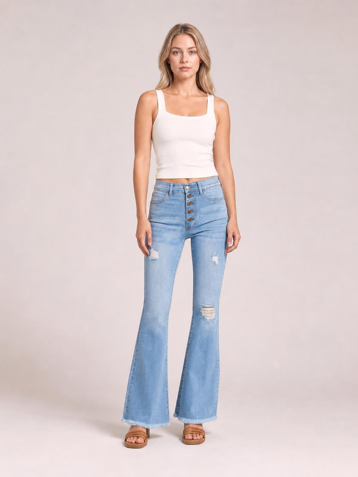 Model wears light-wash MIU Jess button flare jeans with an ultra-high rise, five-button fly, distressed knees, fitted hips, and frayed hems.