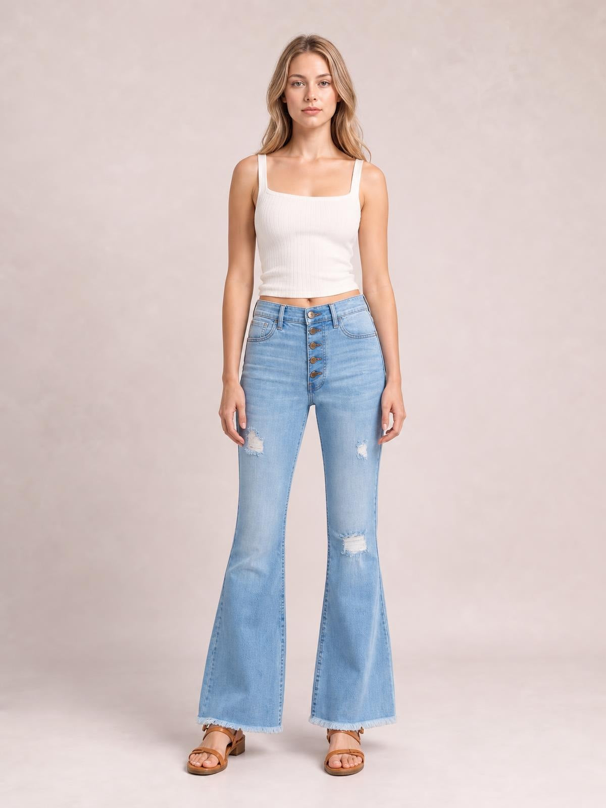 Model stands facing forward in light-wash ultra-high-rise flare jeans with a five-button fly, distressed knees, fitted hips, and frayed hems.