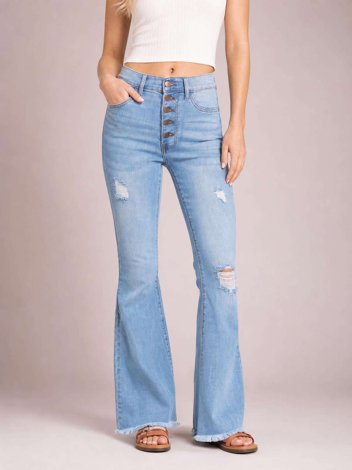 A model wears light-wash MIU Jess ultra-high-rise flare jeans with a five-button fly, distressed knees, fitted hips, and frayed hems.
