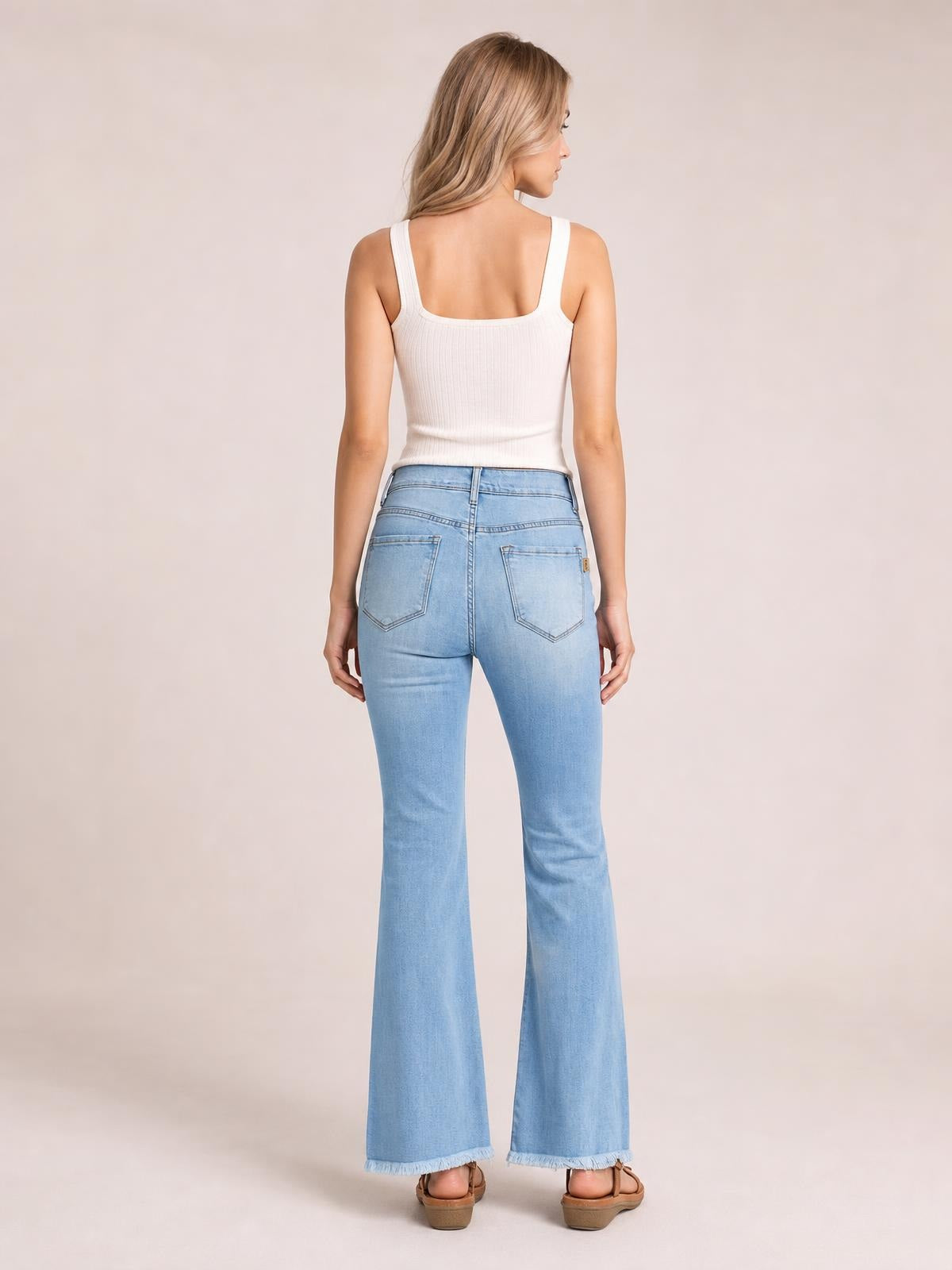 Model shown from behind wearing light-wash, ultra-high-rise flare jeans with fitted hips, back patch pockets, subtle distressing, and frayed hems.