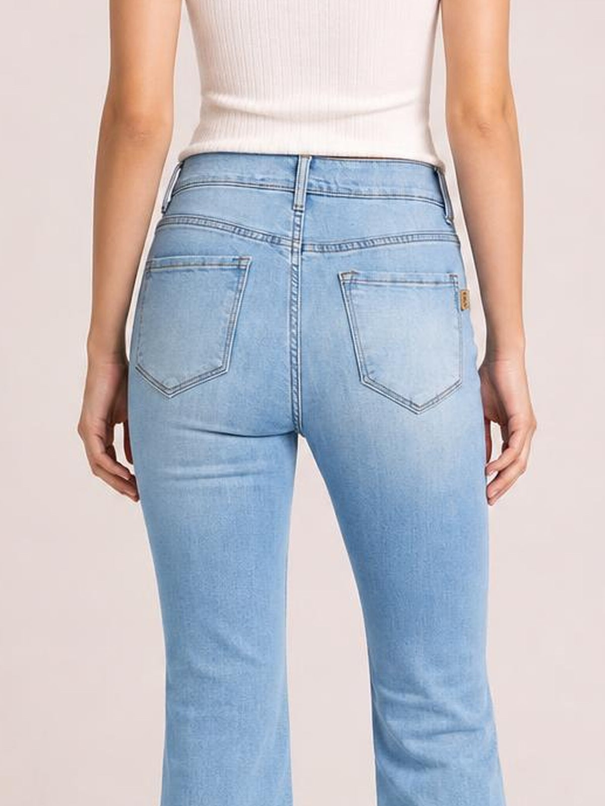 A model stands facing away in light-blue ultra-high-rise flare jeans with back patch pockets, contrast stitching, and a fitted silhouette through the hips and thighs.