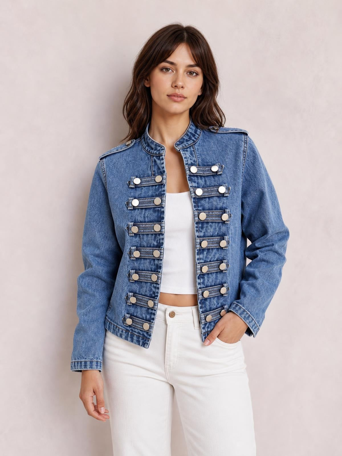 A model poses in a washed blue denim jacket with an open front, stand collar, shoulder epaulettes, long sleeves, and decorative buttoned tabs.