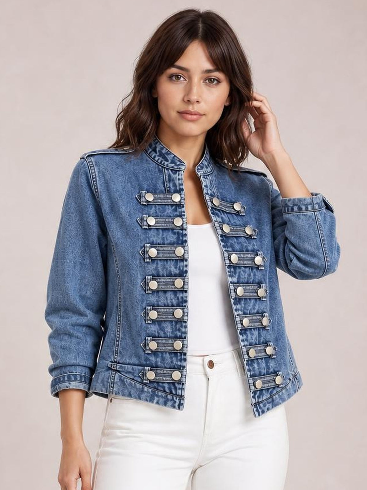 A model poses in a washed blue vintage open-front denim jacket with a stand collar, long sleeves, and decorative buttoned tabs in a structured silhouette.