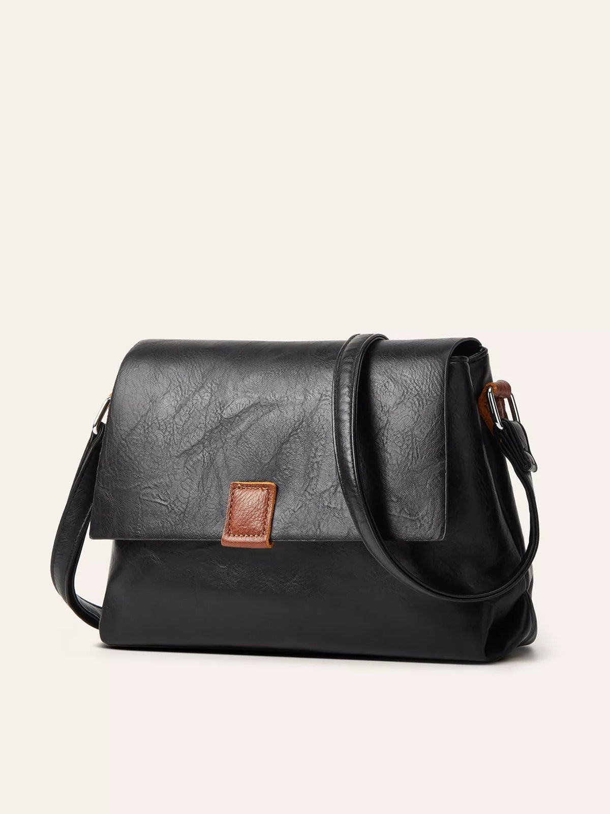 A medium black PU leather crossbody bag with a structured rectangular silhouette, flap closure, long strap, and contrasting brown tab detail.