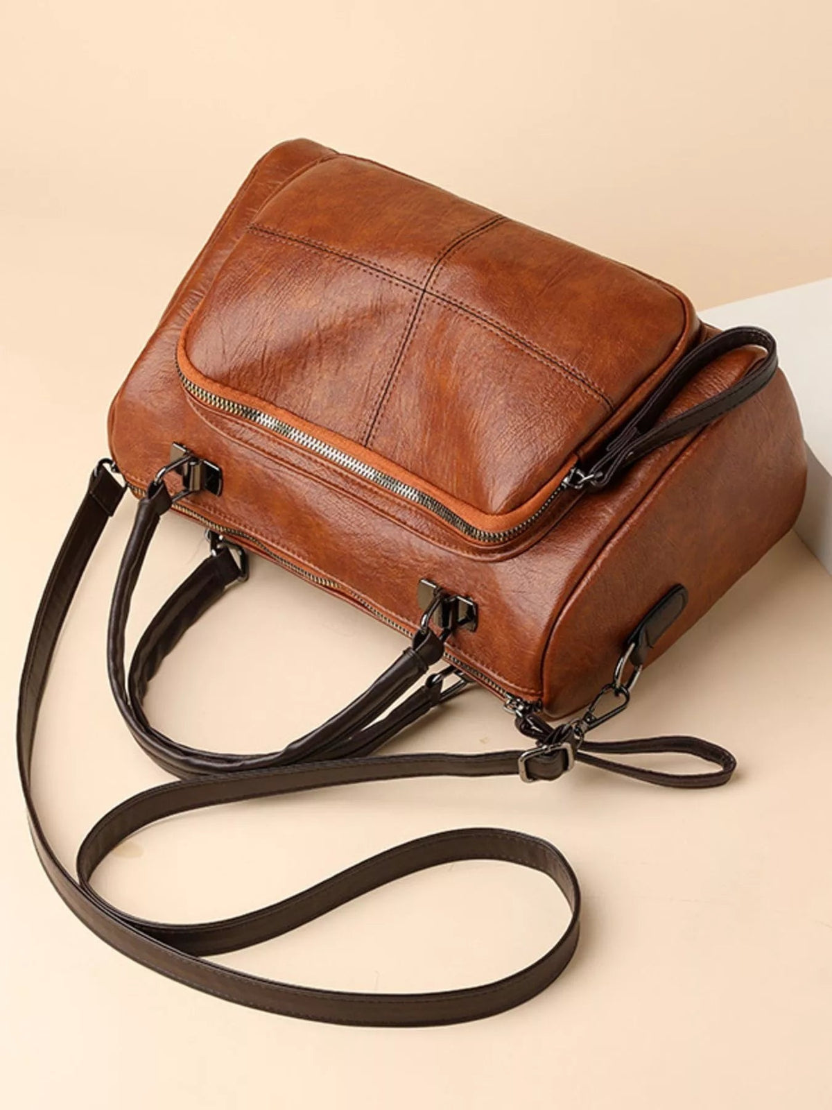 Medium brown vintage-style PU leather crossbody bag with a structured rectangular silhouette, stitched flap, silver zippers, short handles, and a detachable long strap.
