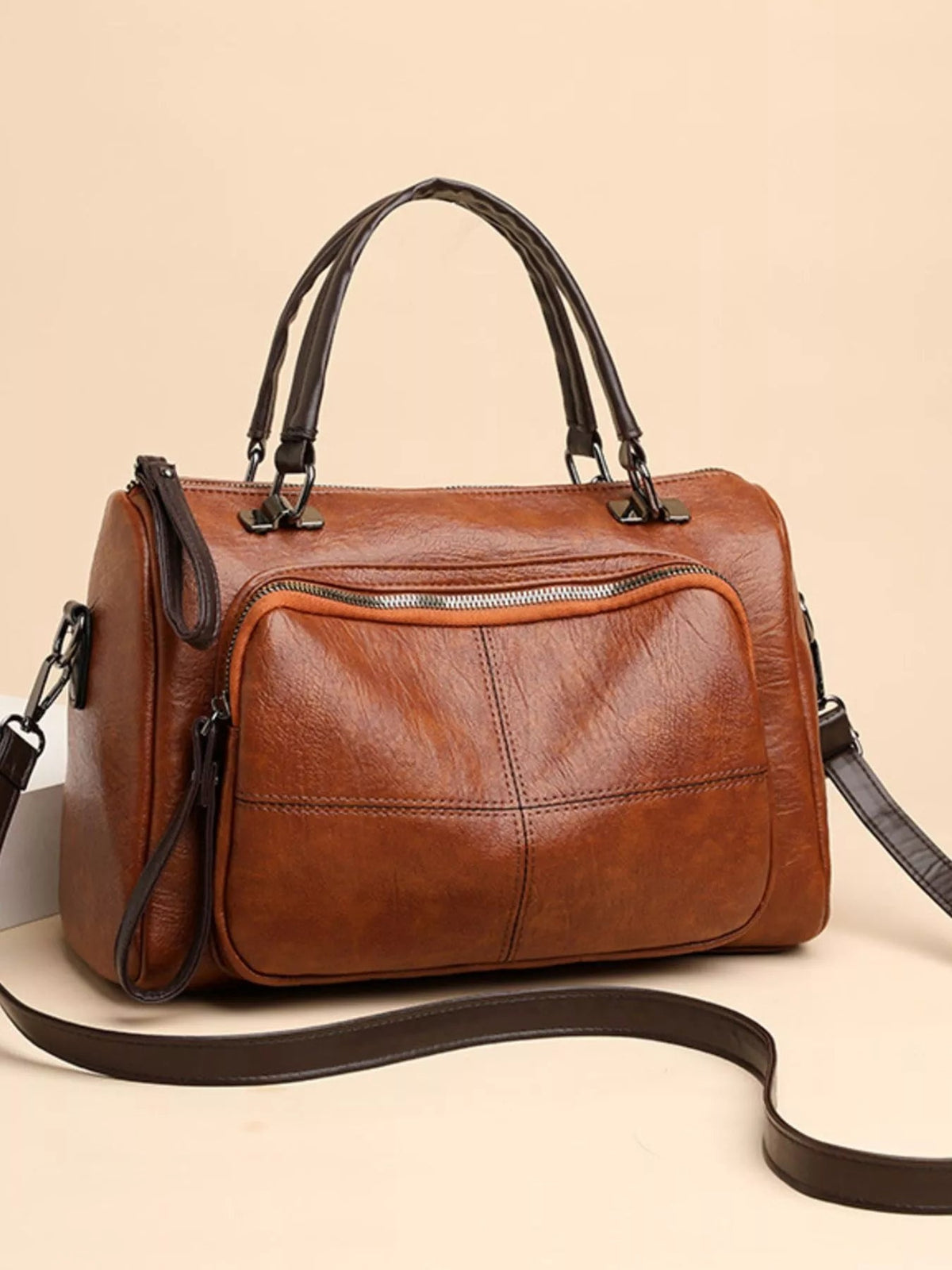 Medium brown vintage-style PU leather crossbody bag with structured silhouette, dual top handles, front zip pocket, stitched panels, and detachable shoulder strap.