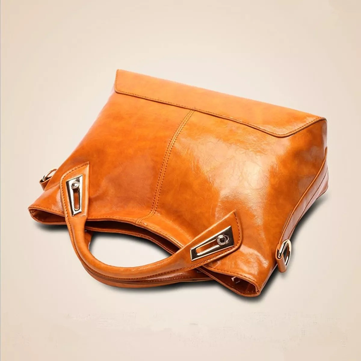 Vintage-style medium PU leather tote handbag in glossy caramel brown, featuring stitched panels, a flap top, dual handles, metal hardware, and an adjustable shoulder strap.