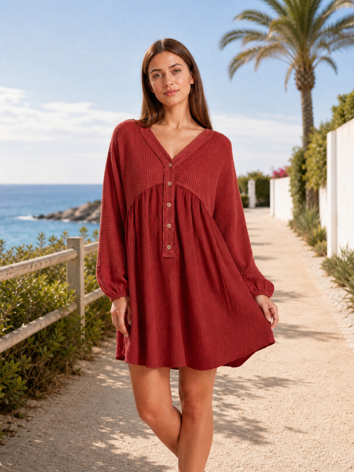 A model stands in a red waffle-knit contrast mini dress with a V-neck, half-button front, long gathered-cuff sleeves, and a softly flowing gathered waist.