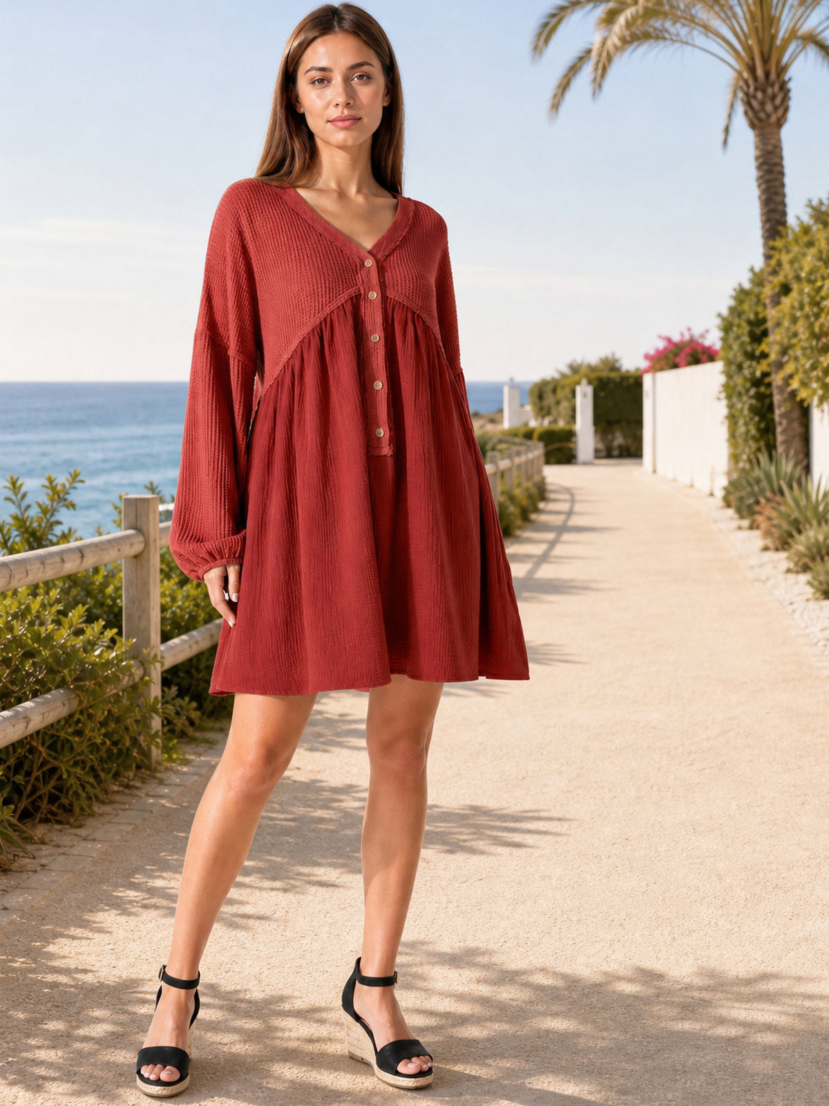 A model stands with one leg crossed in a red waffle-knit contrast mini dress featuring a V-neck, half-button front, long sleeves, gathered cuffs, and a flowing silhouette.