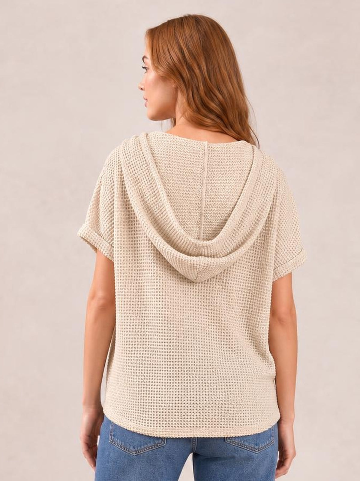 Model shown from the back wears a cream waffle-knit hooded short-sleeve top with a relaxed silhouette, dropped sleeves, and rounded hem.