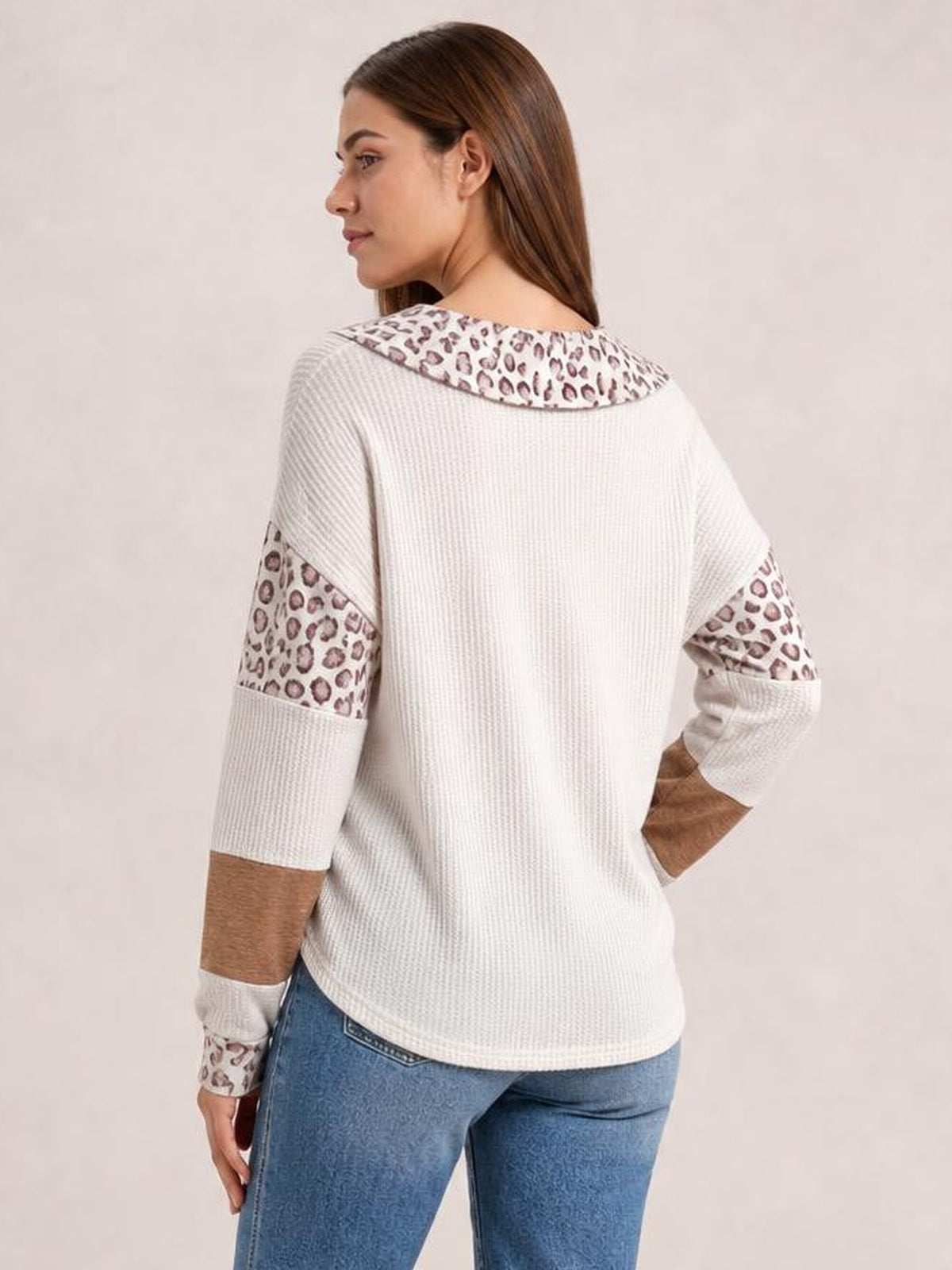 A model poses turned away in a relaxed white waffle-knit long-sleeve top with a leopard-print Johnny collar and matching sleeve panels.