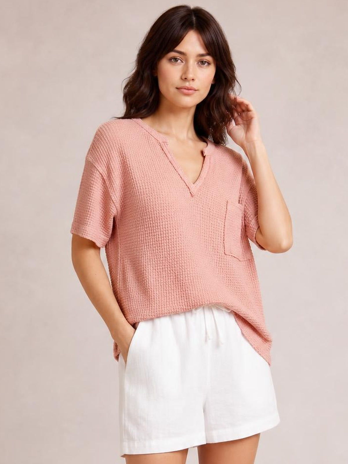 Model wearing a dusty pink waffle-knit T-shirt with a notched V-neck, half sleeves, relaxed silhouette, and visible chest pocket, posing with one hand in her shorts pocket.
