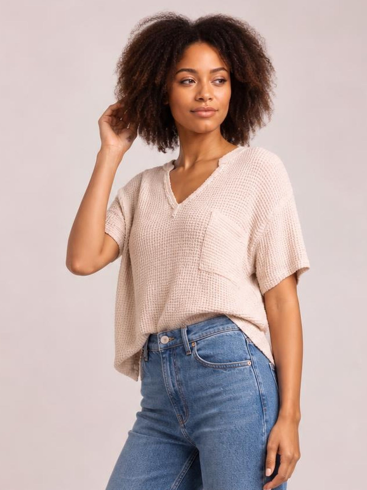 Model poses in a light beige waffle-knit T-shirt with a notched neckline, half sleeves, relaxed silhouette, and visible front pocket.