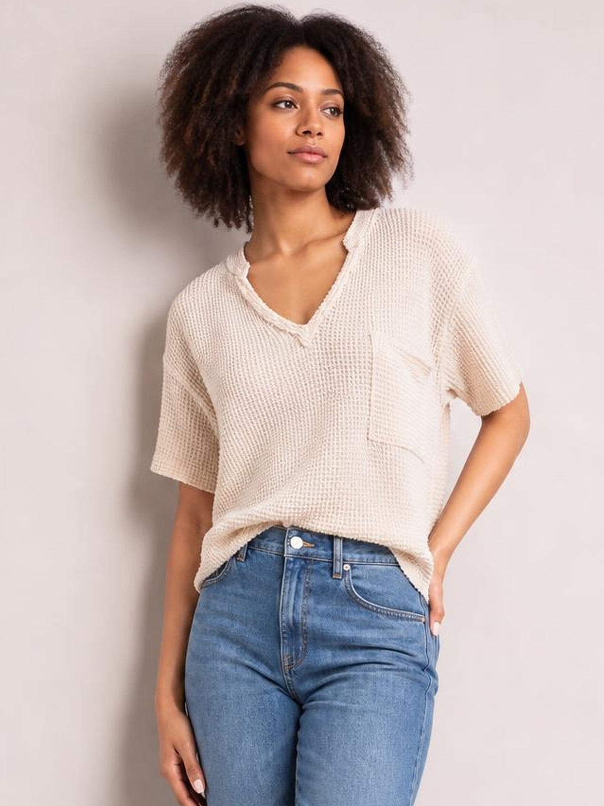 A model wears an ivory waffle-knit T-shirt with a notched neckline, half sleeves, chest pocket, and relaxed straight silhouette.