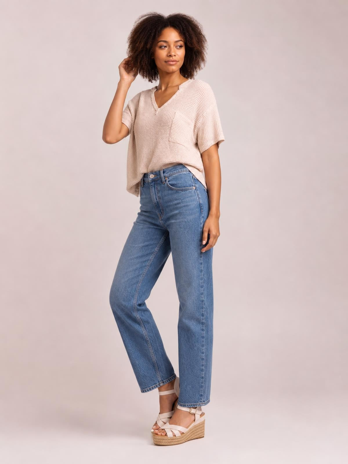Model poses in a blush waffle-knit half-sleeve T-shirt with a notched neckline, chest pocket, relaxed silhouette, and raw-edge construction.