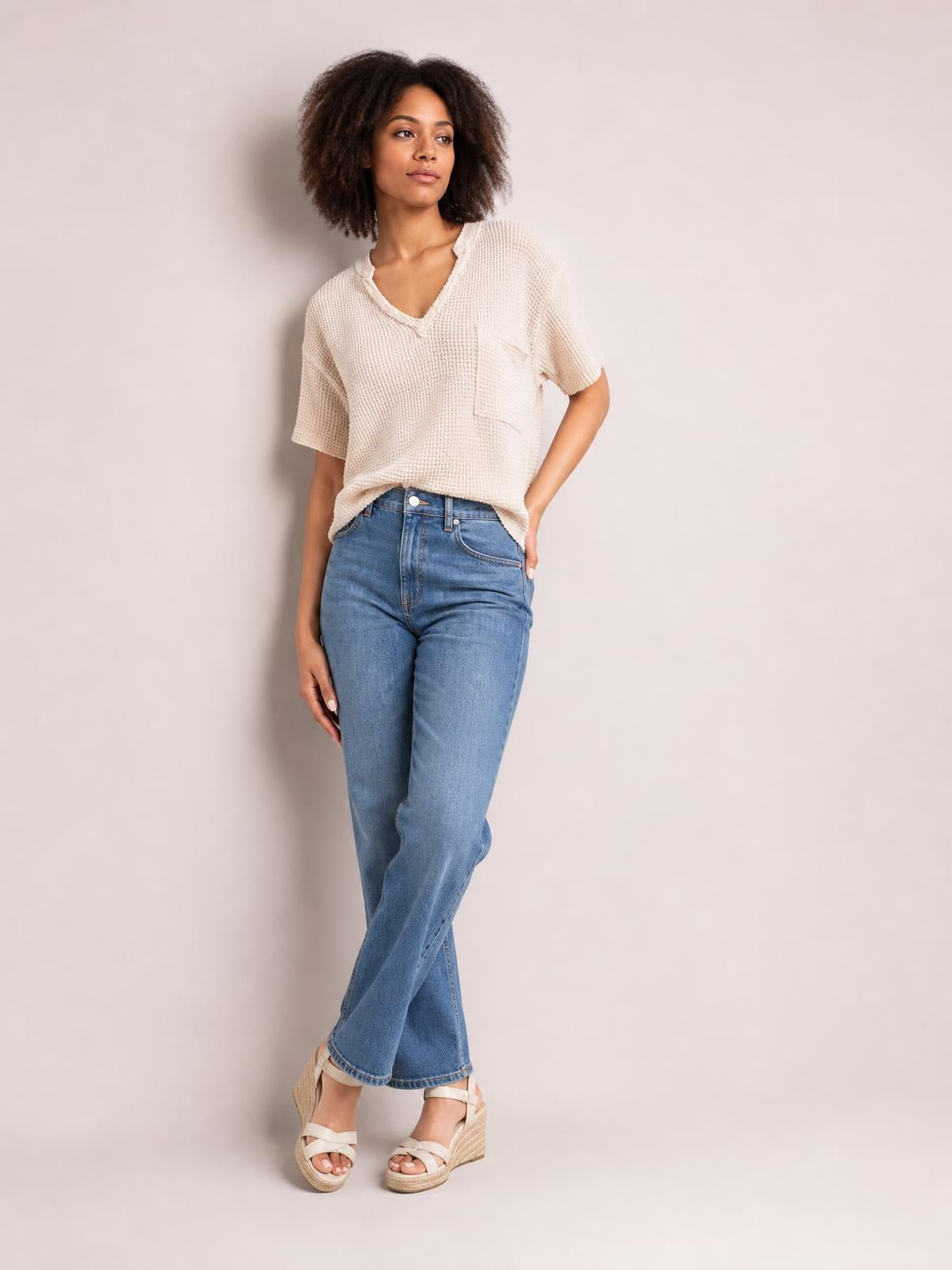 Model wears an ivory waffle-knit notched half-sleeve T-shirt with a relaxed silhouette and chest pocket, posed with one hand in her jeans pocket.