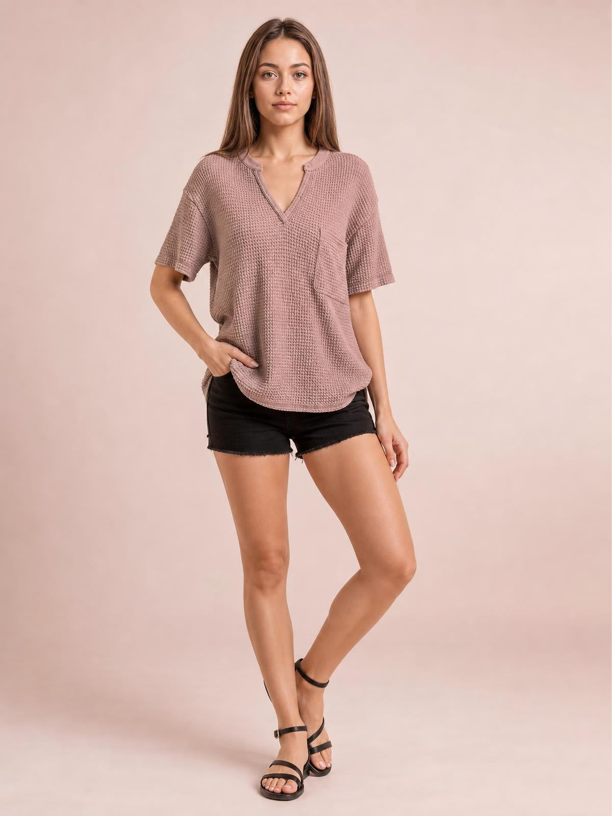 Model poses with one hand at her hip wearing a dusty rose waffle-knit T-shirt with a notched neckline, half sleeves, relaxed silhouette, and visible chest pocket.