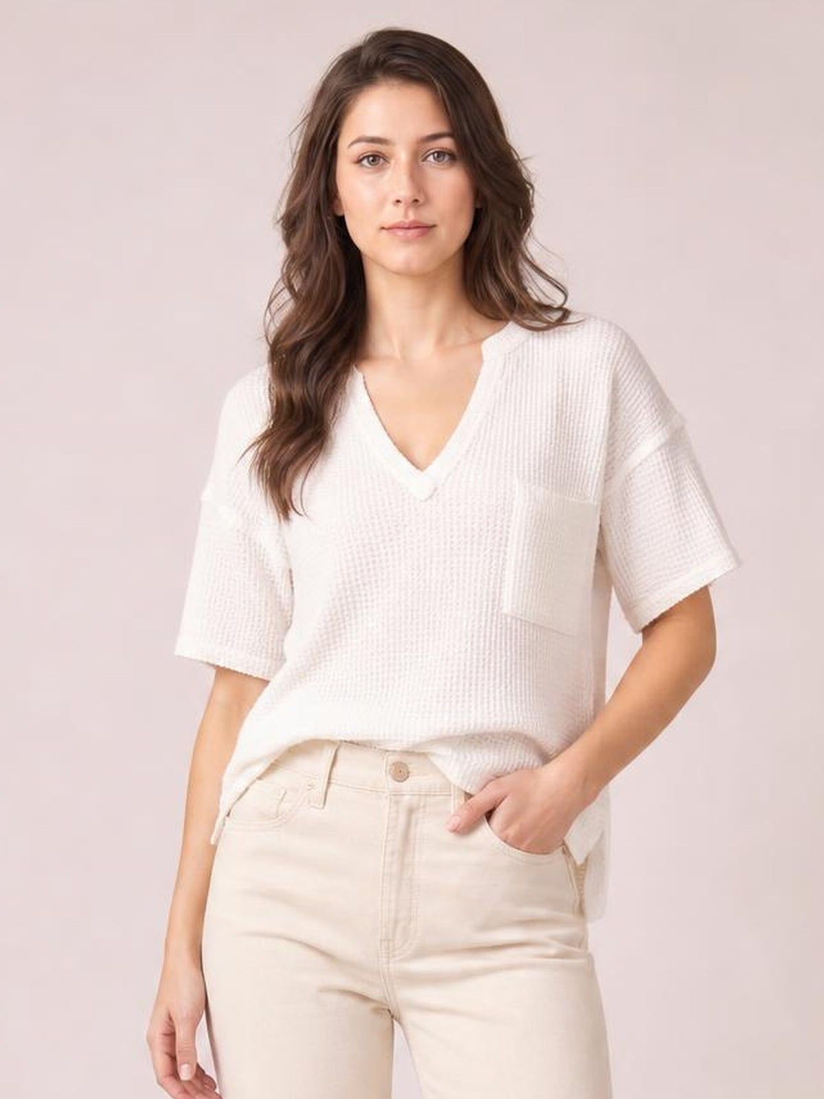 Model poses in a white waffle-knit T-shirt with a notched V-neck, relaxed silhouette, half sleeves, and a visible front pocket.