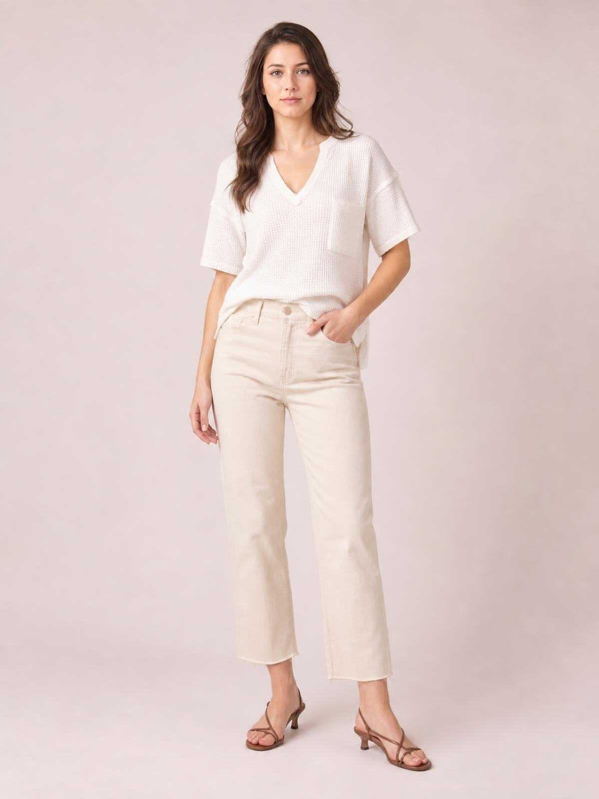 Model wears a white waffle-knit T-shirt with a notched V-neck, half sleeves, chest pocket, and relaxed silhouette while standing with one hand in her pocket.