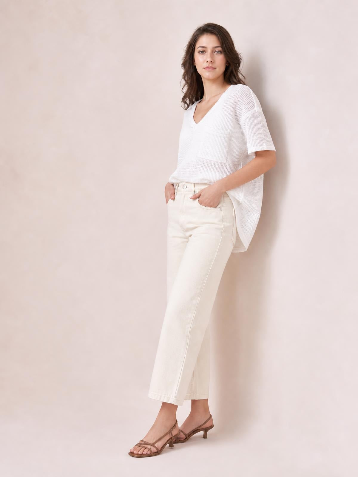Model wears a white waffle-knit notched half-sleeve T-shirt with a relaxed tunic silhouette and visible chest pocket, hands resting in trouser pockets.