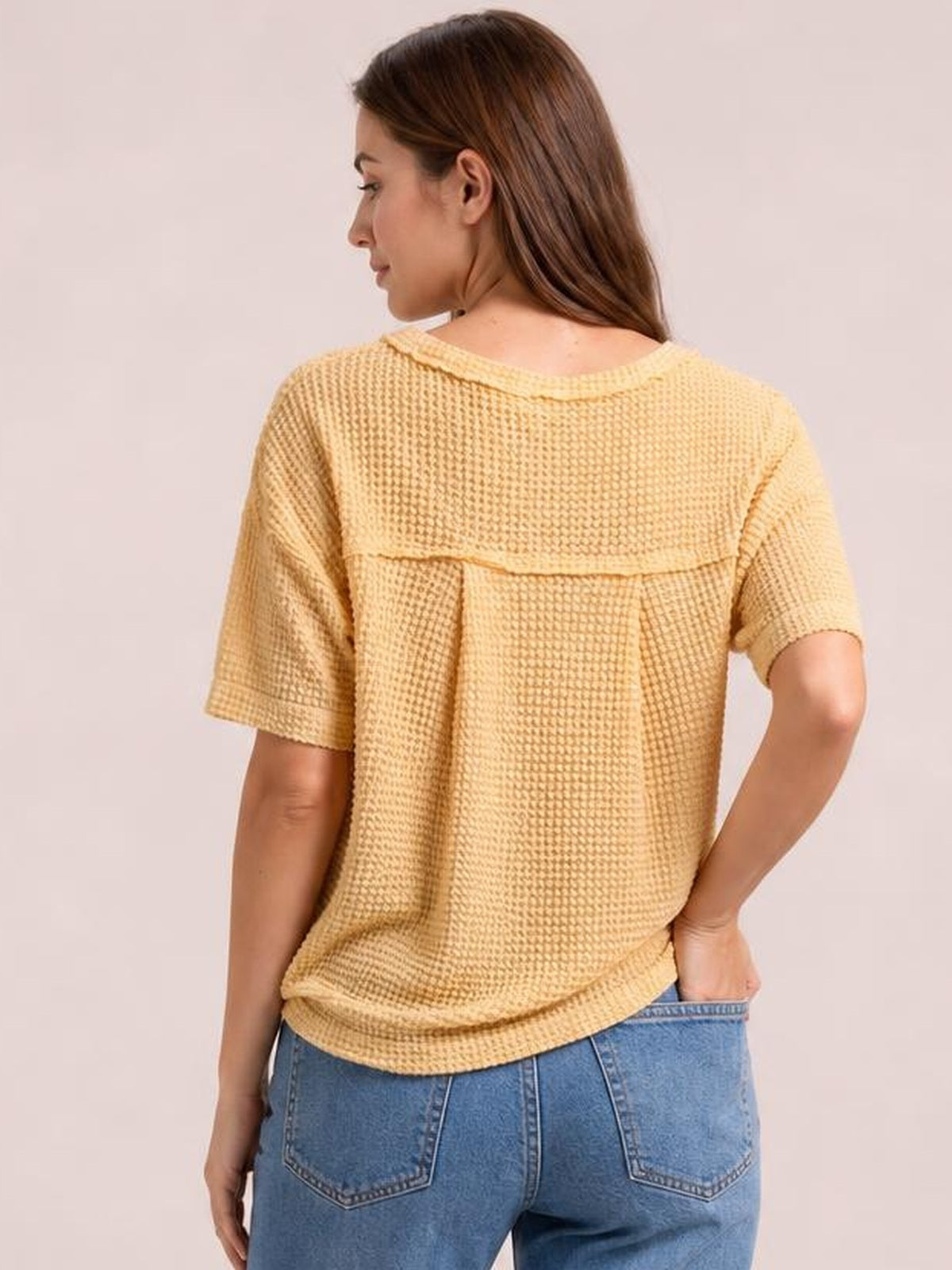 Back view of a model wearing a loose pale yellow waffle-knit T-shirt with half sleeves, a rounded neckline, and a relaxed straight silhouette.
