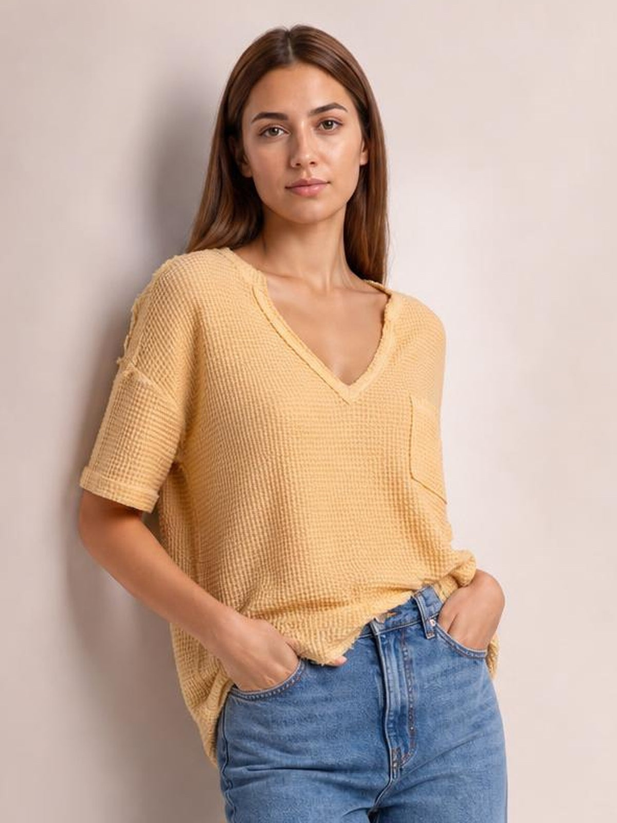 Model wears a camel waffle-knit T-shirt with a notched V-neck, relaxed silhouette, half sleeves, and a visible chest pocket, posing with hands in jeans pockets.