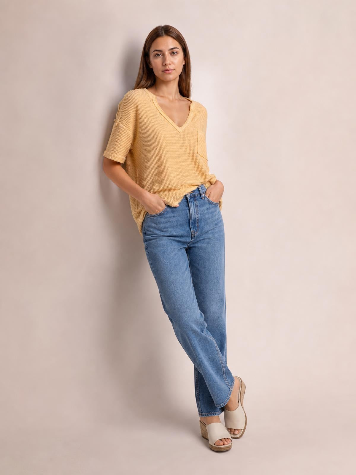 A model wears a tan waffle-knit T-shirt with a notched neckline, half sleeves, chest pocket, and relaxed silhouette while standing with hands in jean pockets.