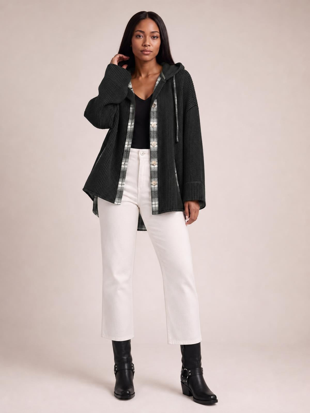 A woman poses in a relaxed black waffle-knit hooded shacket with plaid patchwork panels, button front, drawstrings, long sleeves, and a loose silhouette.