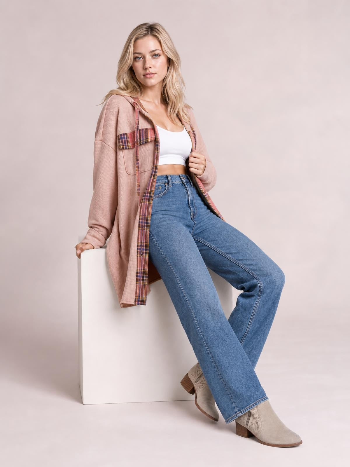 A model sits in a relaxed pose wearing a dusty pink waffle knit plaid patchwork hooded shacket with an open front, pockets, and relaxed silhouette.