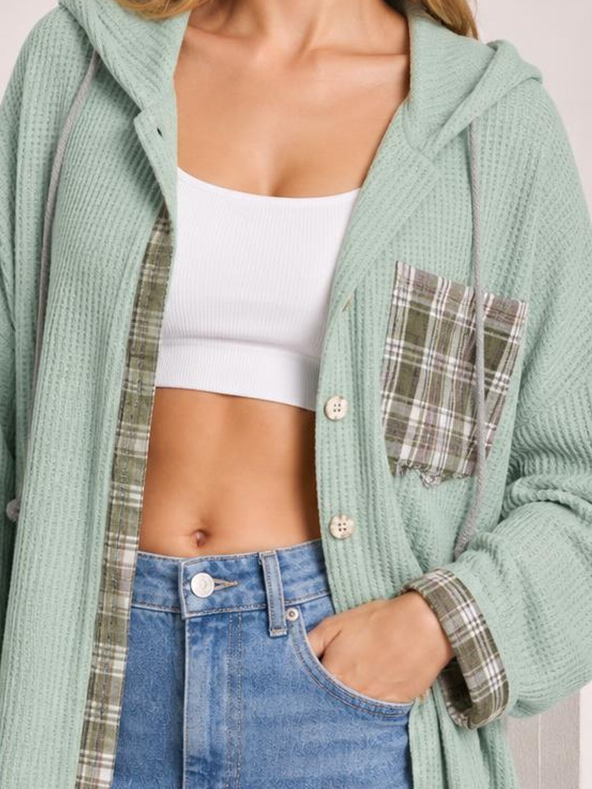 Model wears an open mint waffle knit hooded shacket with plaid patchwork panels, button front, and a relaxed silhouette, posing with one hand in a pocket.
