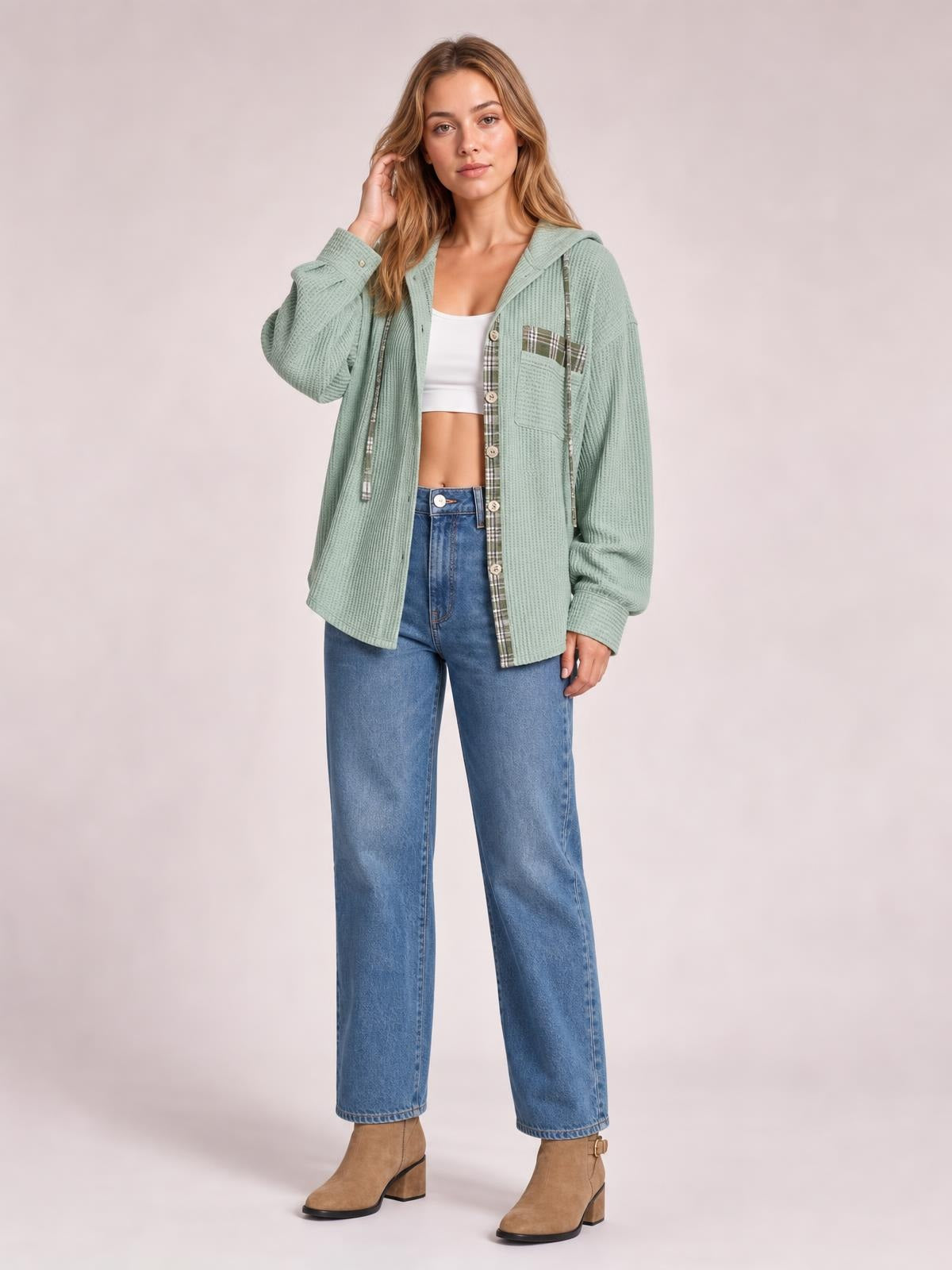 A model poses in a sage green waffle knit hooded shacket with plaid patchwork trim, drawstrings, button front, long sleeves, and a relaxed silhouette.