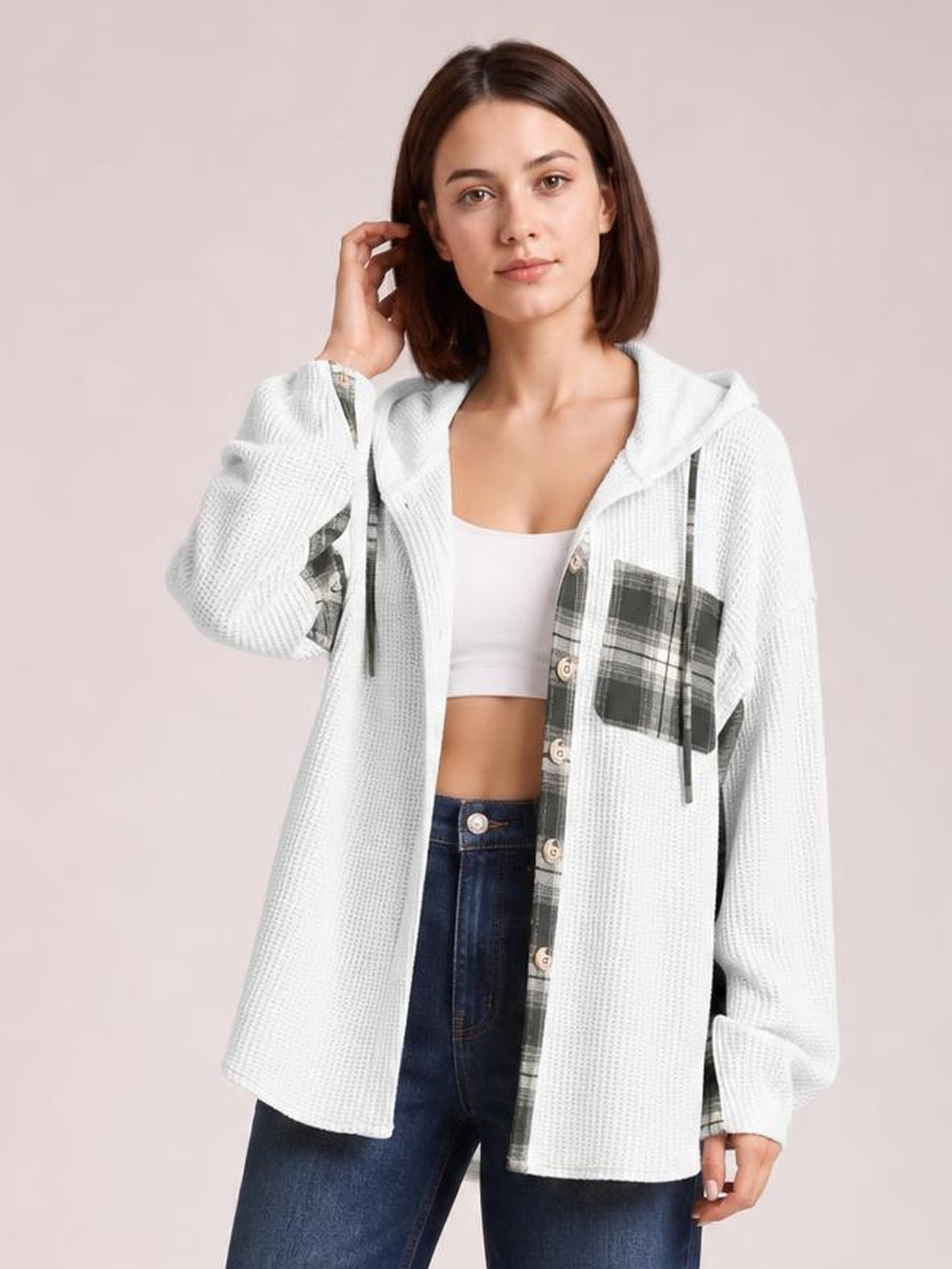 A woman poses in a white waffle knit hooded shacket with gray plaid patchwork panels, drawstrings, button front, chest pocket, and a relaxed silhouette.