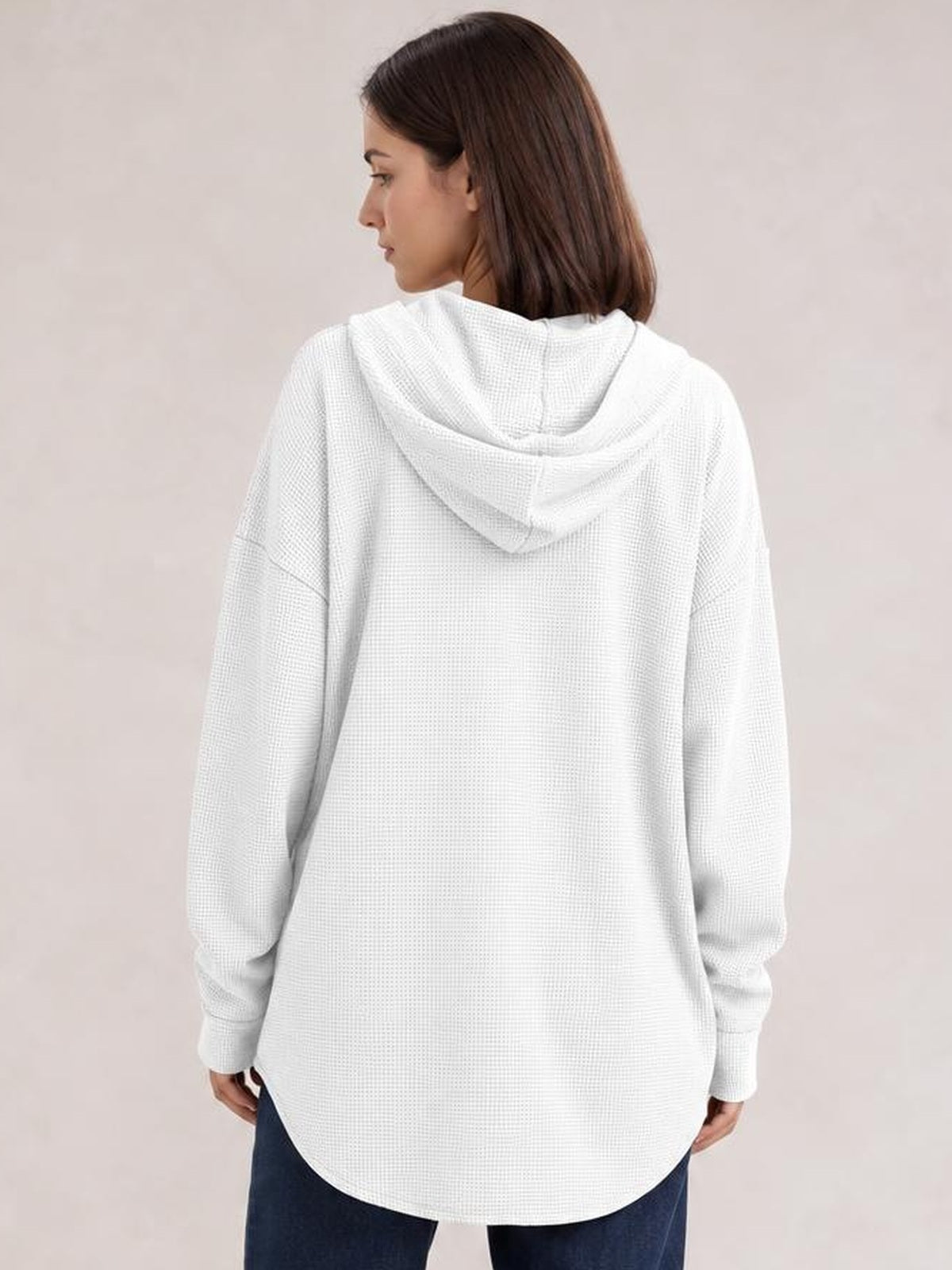 A woman models the back of a white waffle-knit hooded shacket with a relaxed oversized silhouette, long sleeves, ribbed cuffs, and a curved hem.