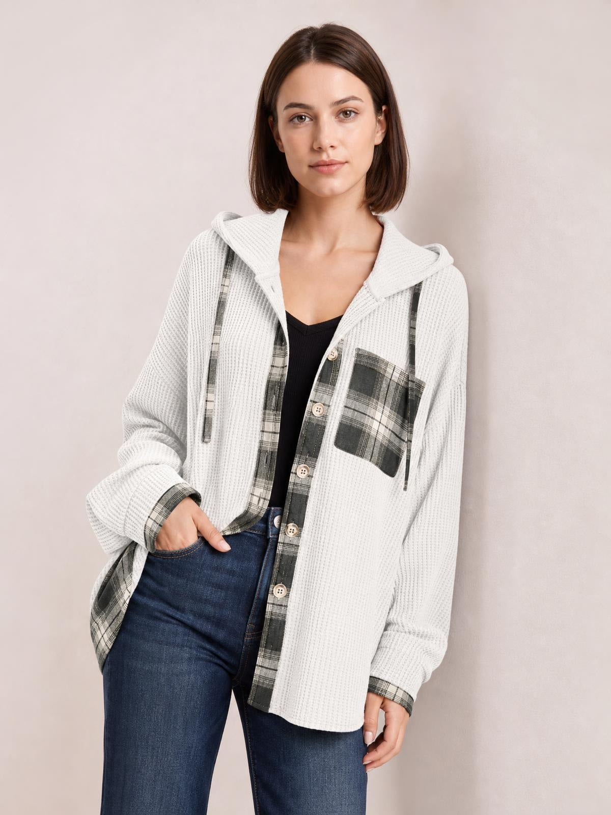 A woman poses with one hand in her jeans pocket, wearing a white waffle knit hooded shacket with gray plaid patchwork, button front, and chest pocket.
