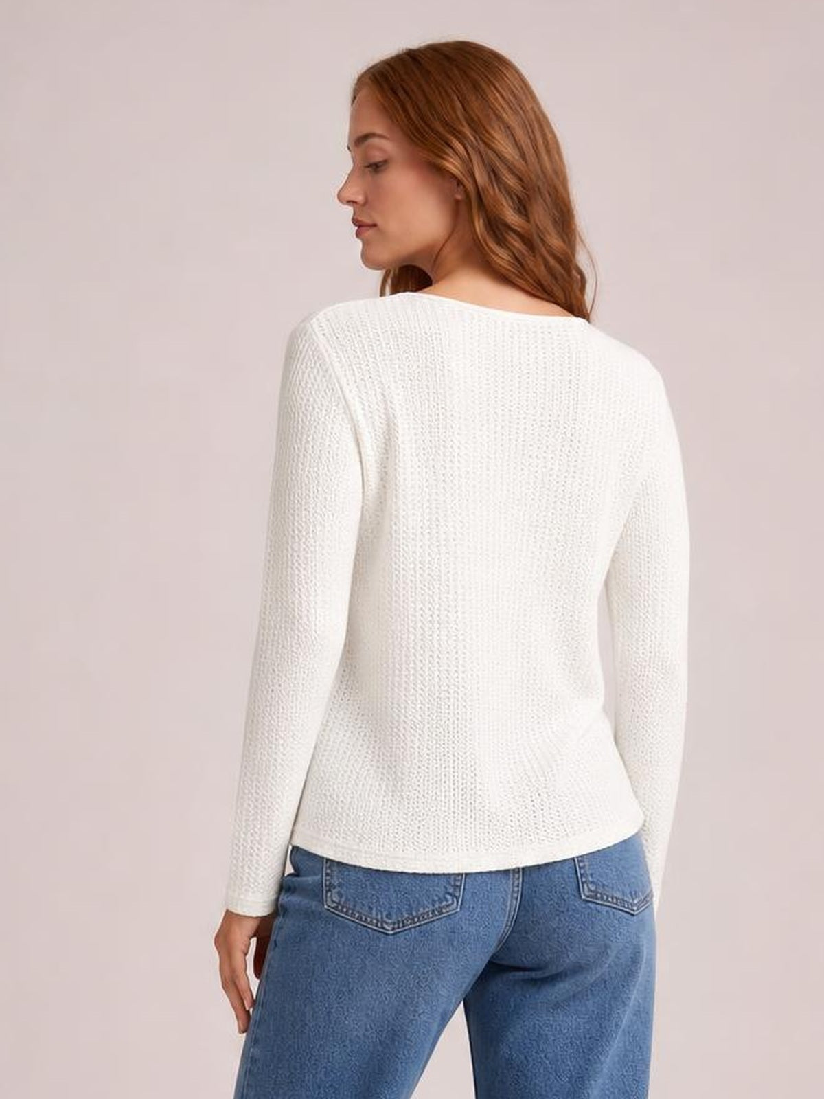 A model looks over her shoulder while wearing a white waffle-knit long sleeve top with a softly fitted silhouette and straight hem.