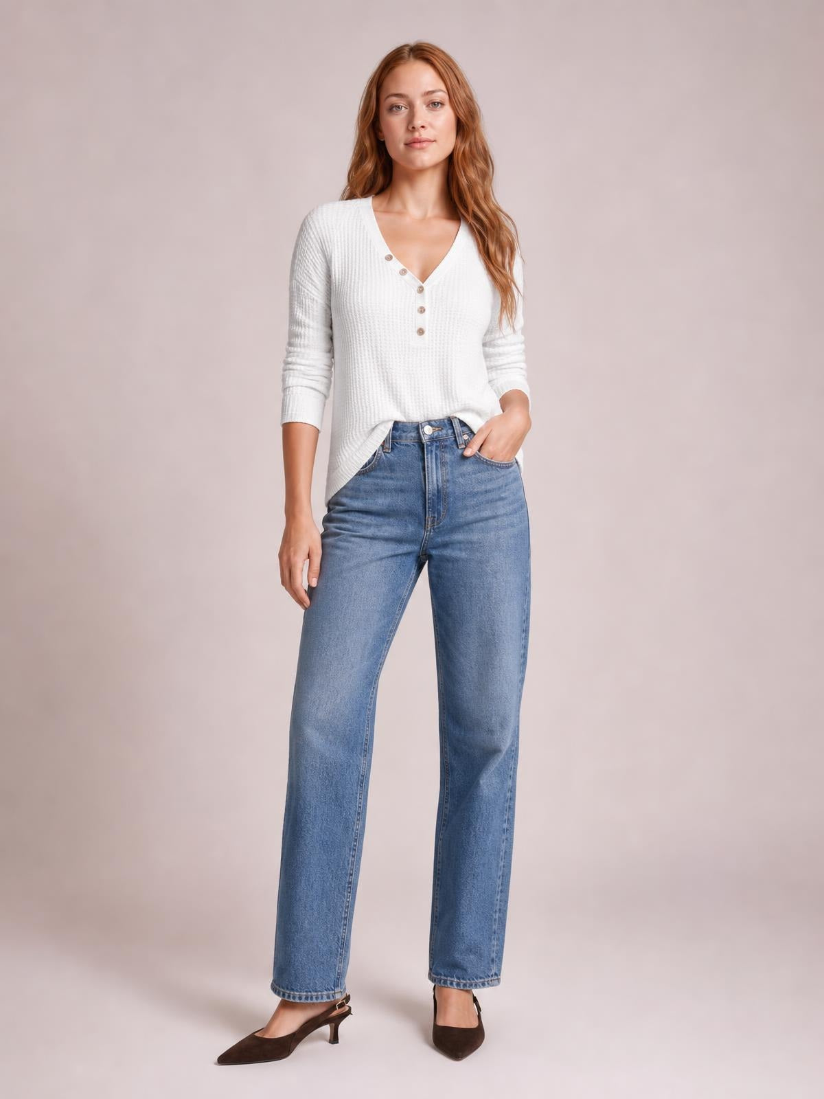 Model poses in a white waffle-knit V-neck long sleeve top with button details and a relaxed silhouette, paired with blue wide-leg jeans.