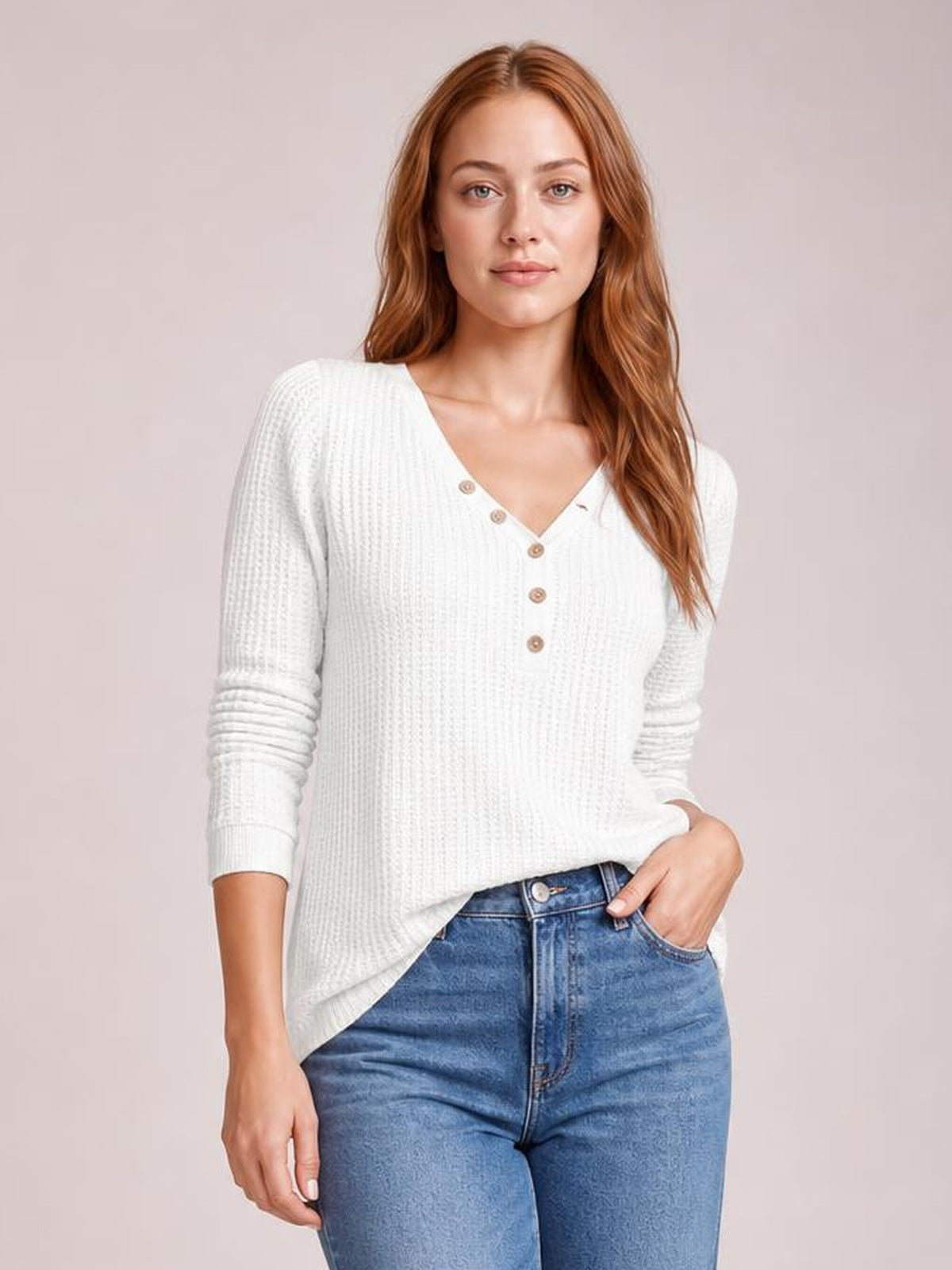 Model wearing an opaque white waffle-knit V-neck long-sleeve top with button details and a relaxed silhouette, posing with one hand in her jeans pocket.