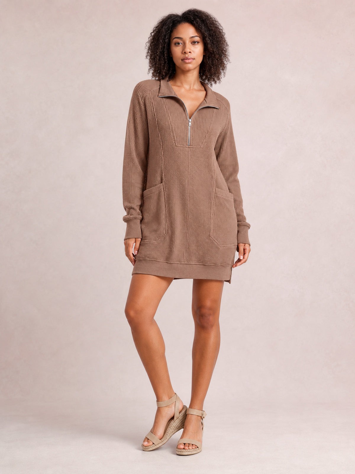 Model wearing a taupe waffle-knit long sleeve mini dress with a half-zip collar, relaxed silhouette, side pockets, ribbed cuffs, and above-the-knee hem.