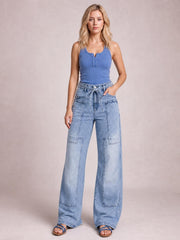 Model wears light-wash wide-leg cargo jeans with a tied waist, oversized patch pockets, and full-length relaxed legs.