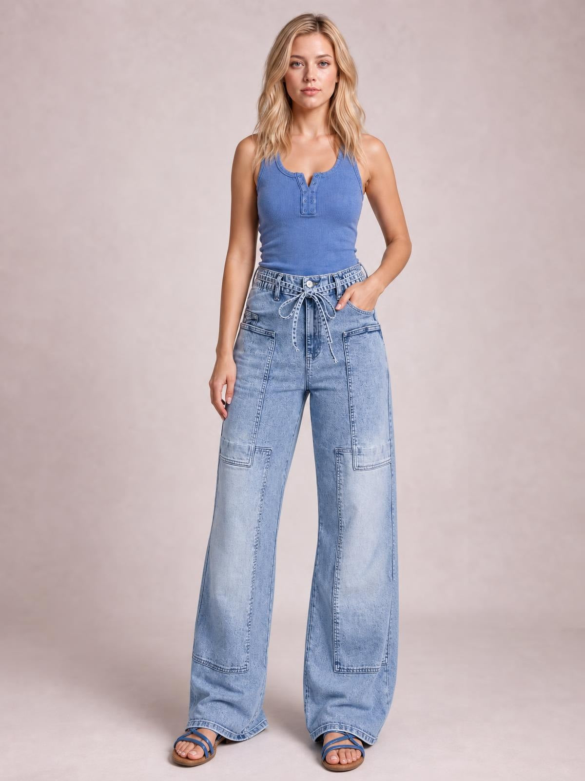Model wears light-wash wide-leg cargo jeans with a tied waist, oversized patch pockets, and full-length relaxed legs.