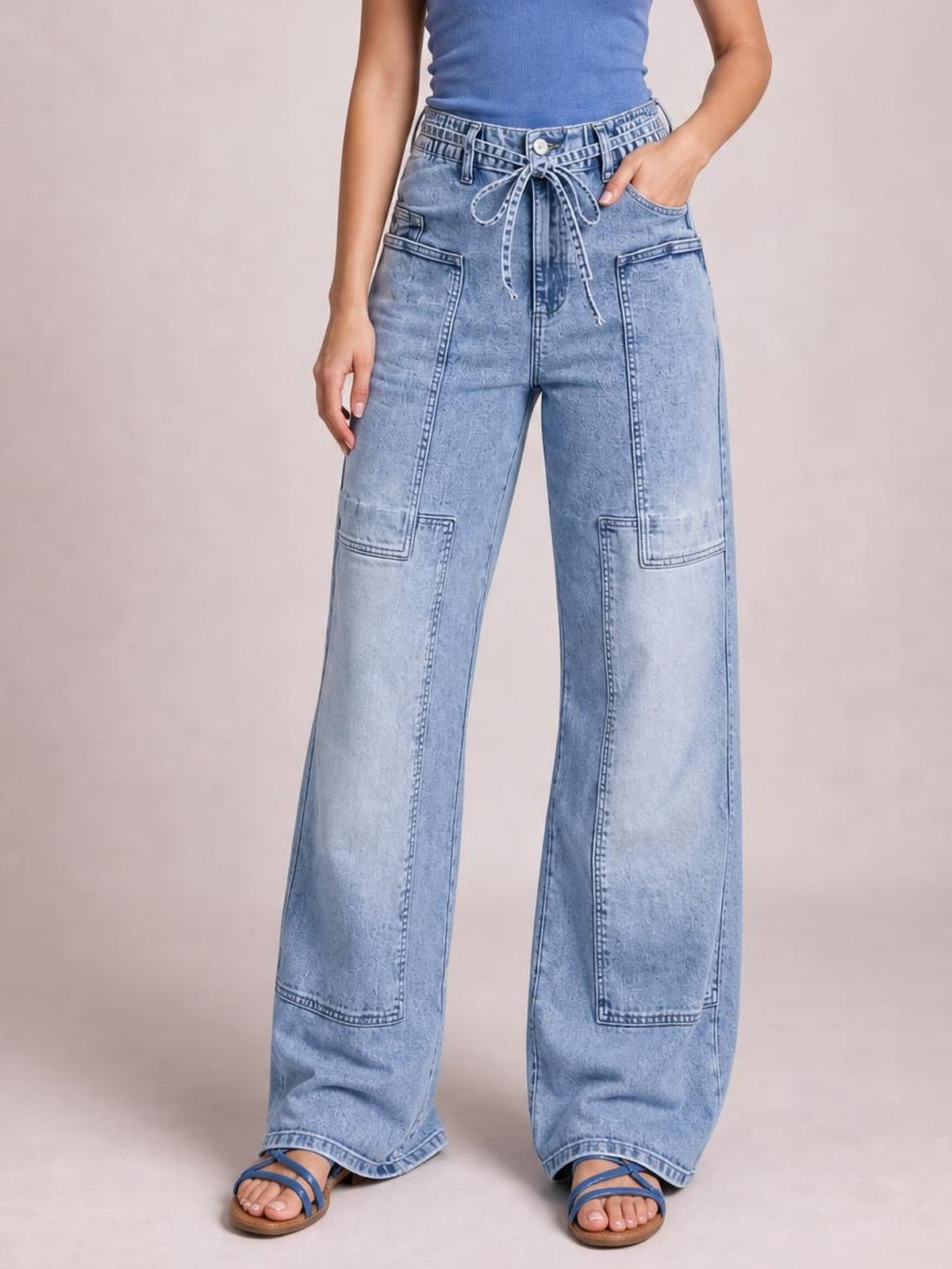 Model wearing light-wash wide-leg cargo jeans with a tied waist, multiple large patch pockets, and full-length panel stitching.