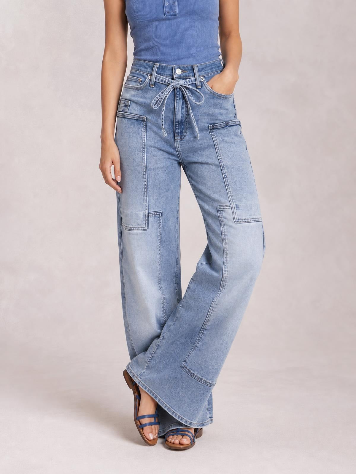 Model wears light-wash wide-leg cargo jeans with a tied waistband, belt loops, front pockets, and large stitched utility pockets.