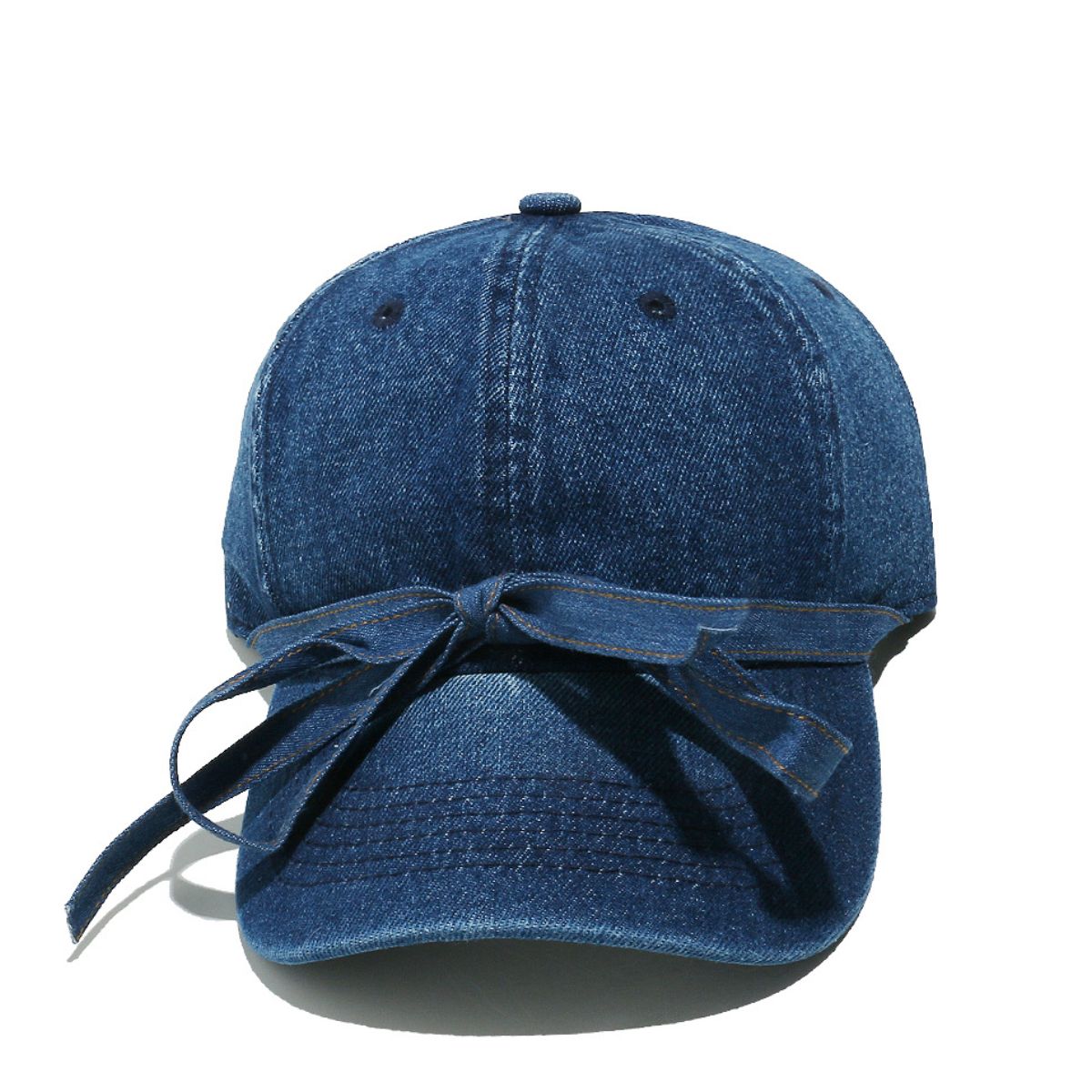 Washed blue denim baseball cap with a classic seamed crown, curved brim, top button, ventilation eyelets, and an oversized front bow with trailing ends.