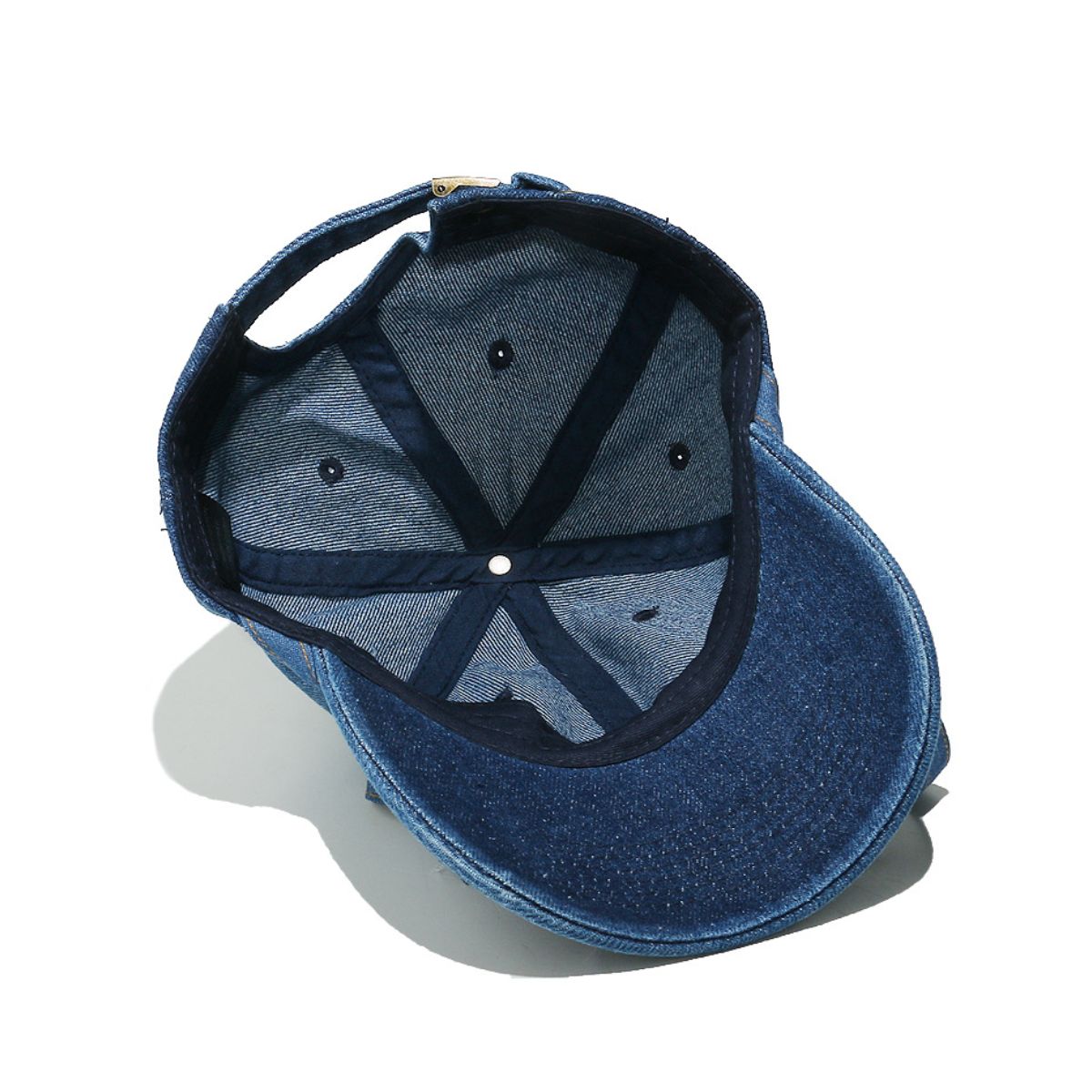 Washed blue denim baseball cap shown from underneath, highlighting its curved brim, seamed cotton crown, ventilation eyelets, and adjustable back strap.